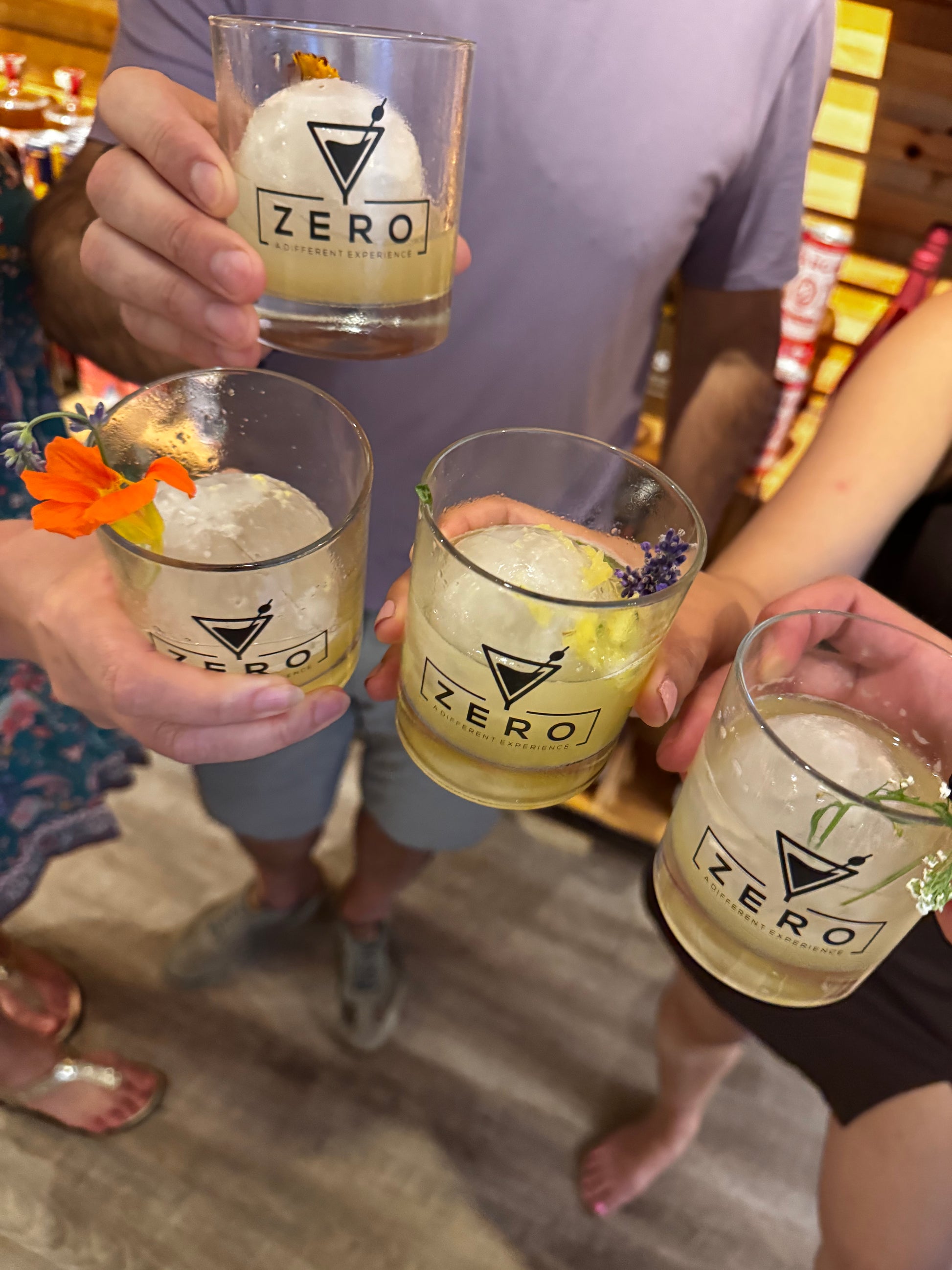 People holding glasses of a beverage with a brand logo, standing on a wooden floor.