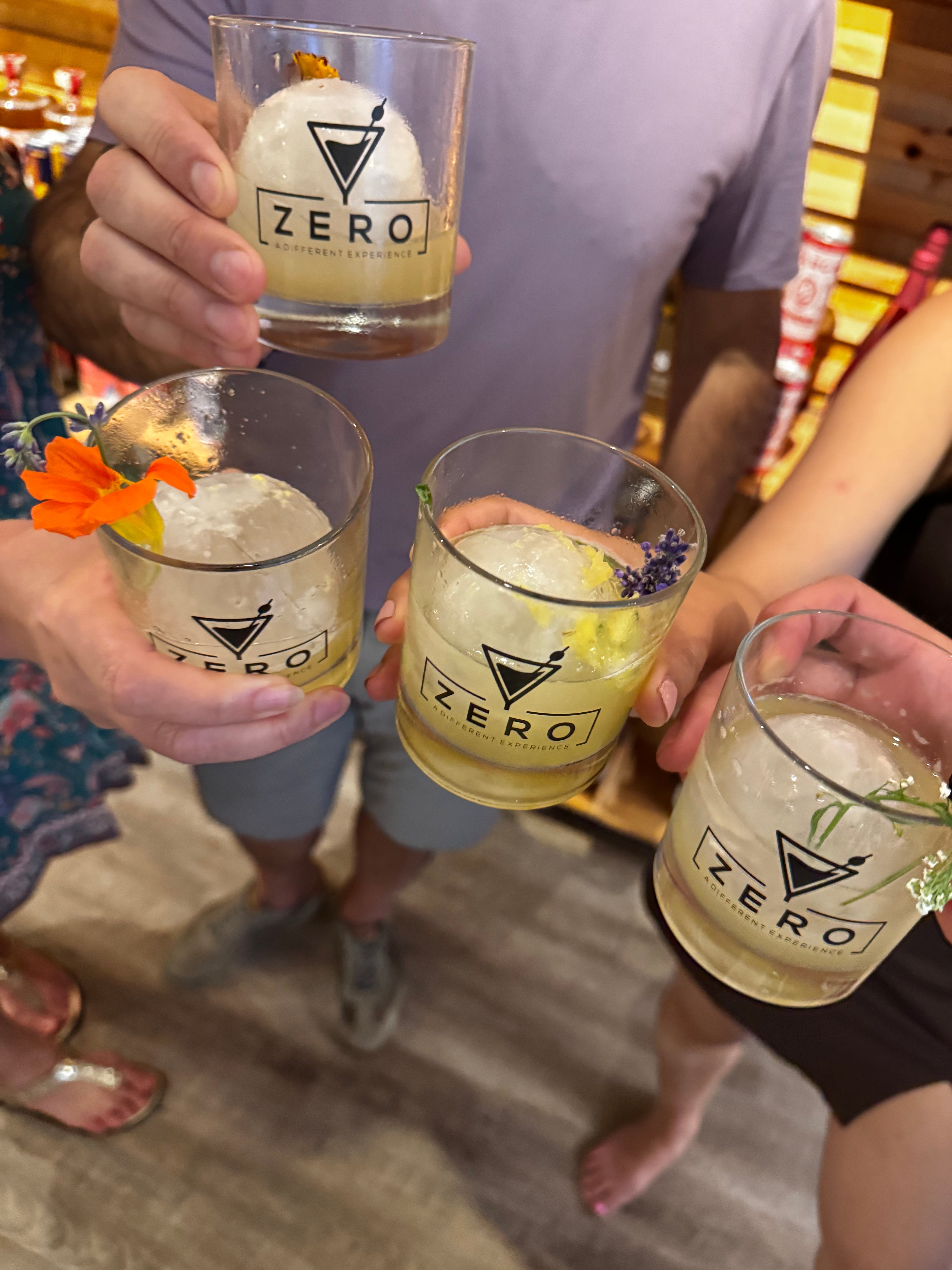 People holding glasses of a beverage with a brand logo, standing on a wooden floor.