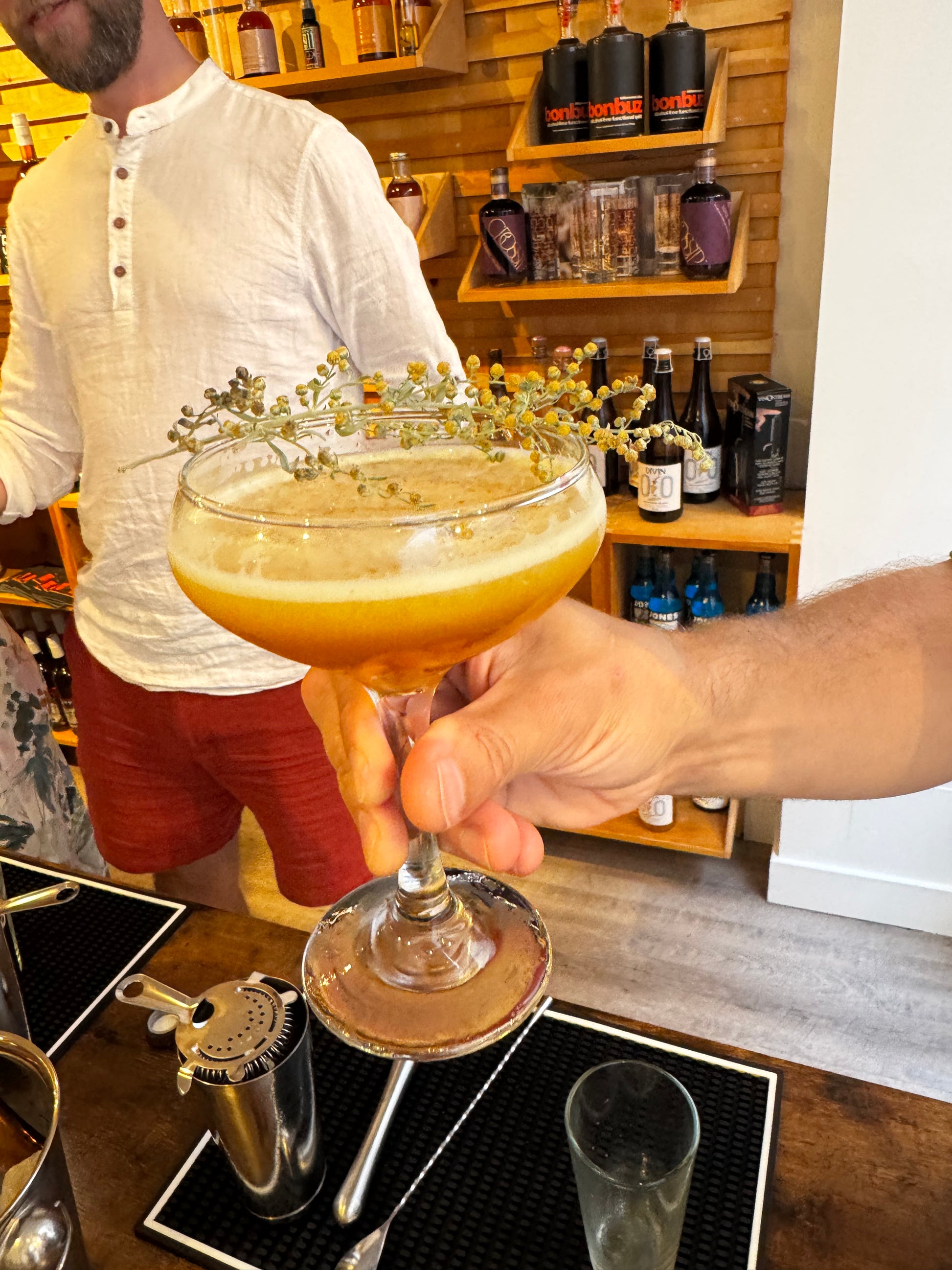 Person pouring a drink from a yellow glass into another glass in a bar setting.