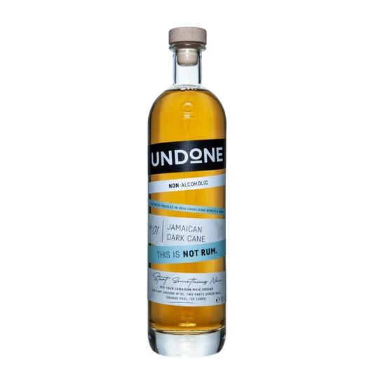 A bottle of Undone Non-Alcoholic Jamaican Dark Cane rum, featuring amber liquid in a clear glass bottle with a black and white label and a light brown wooden cap, set against a plain white background.