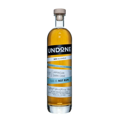 A bottle of Undone Non-Alcoholic Jamaican Dark Cane rum, featuring amber liquid in a clear glass bottle with a black and white label and a light brown wooden cap, set against a plain white background.